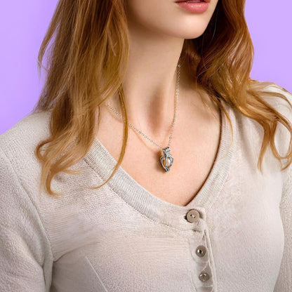 Woman wearing a light gray long-sleeve shirt with a necklace against a purple background